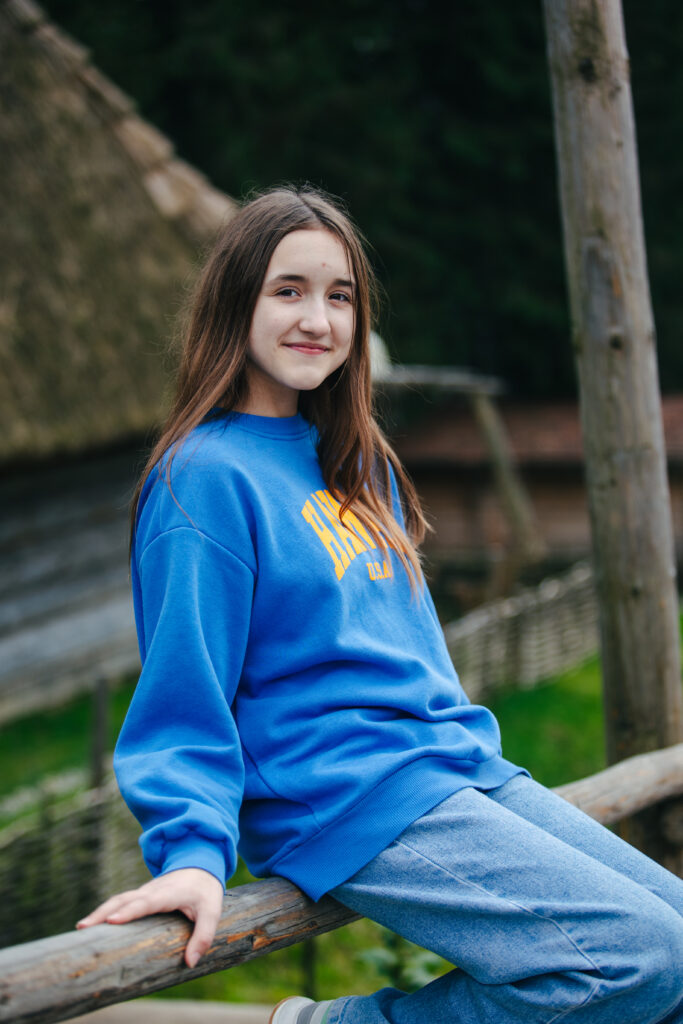 Pige med blå sweatshirt sidder på træhegn.