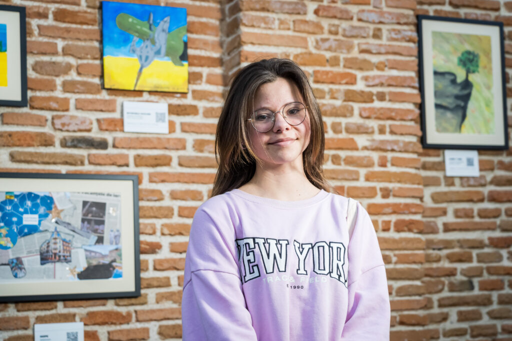 Piger med lilla New York sweatshirt kigger ind i kameraet, i baggrunden er der malerier.